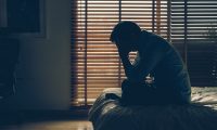 Man in pain sitting on a bed holding is head between his hands